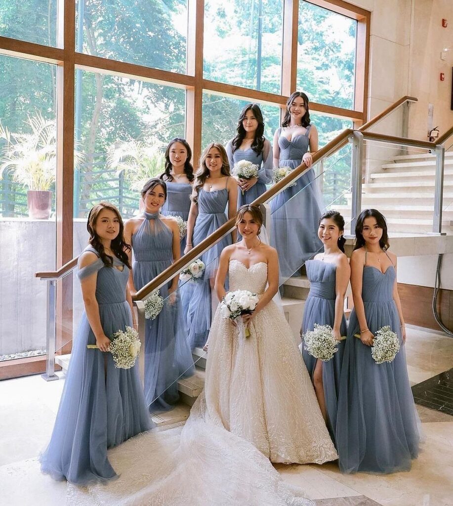 Bridesmaids in dusty blue dresses posing with a bride on a staircase holding white bouquets.