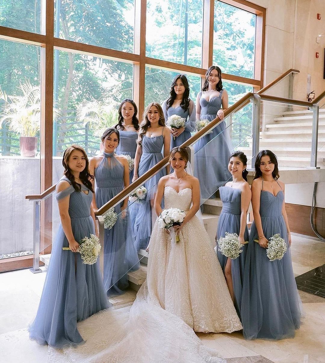 Bridesmaids in dusty blue dresses posing with a bride on a staircase holding white bouquets.