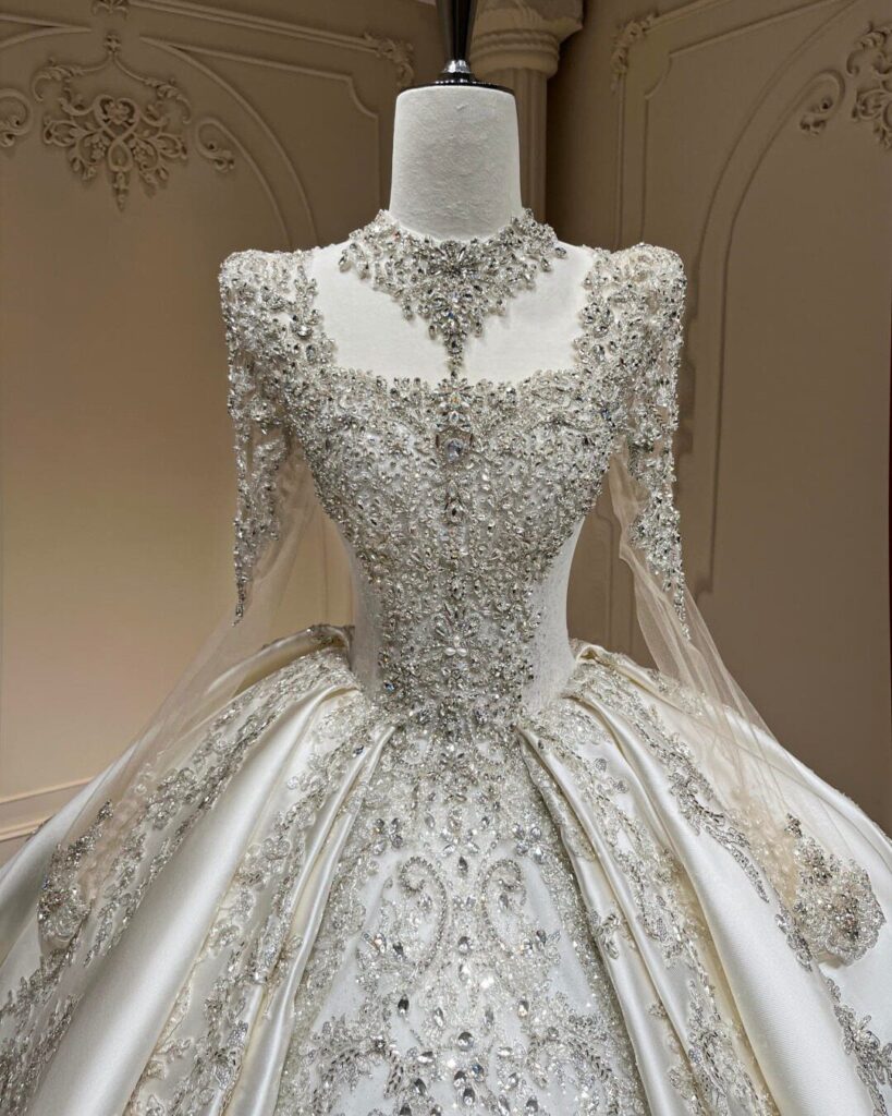 Ornate white wedding dress with heavy crystal embellishments and long sleeves displayed on a mannequin.
