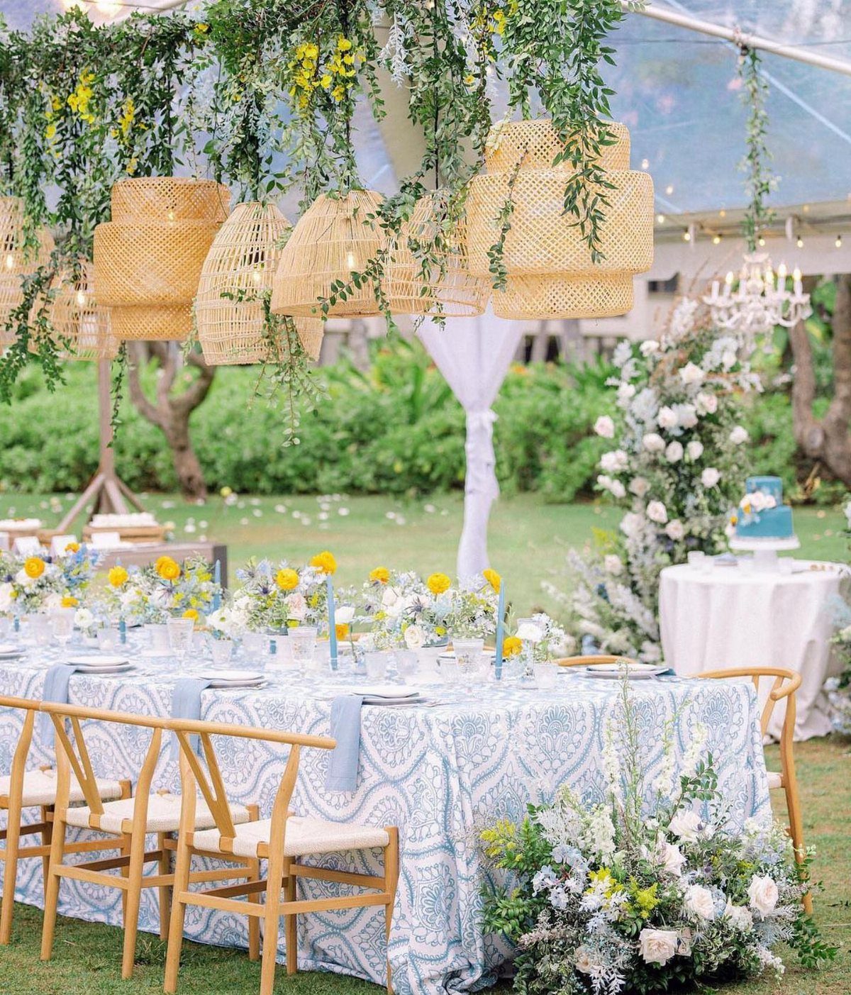 A decorated garden wedding table with blue patterned linens and hanging wicker pendant lights.