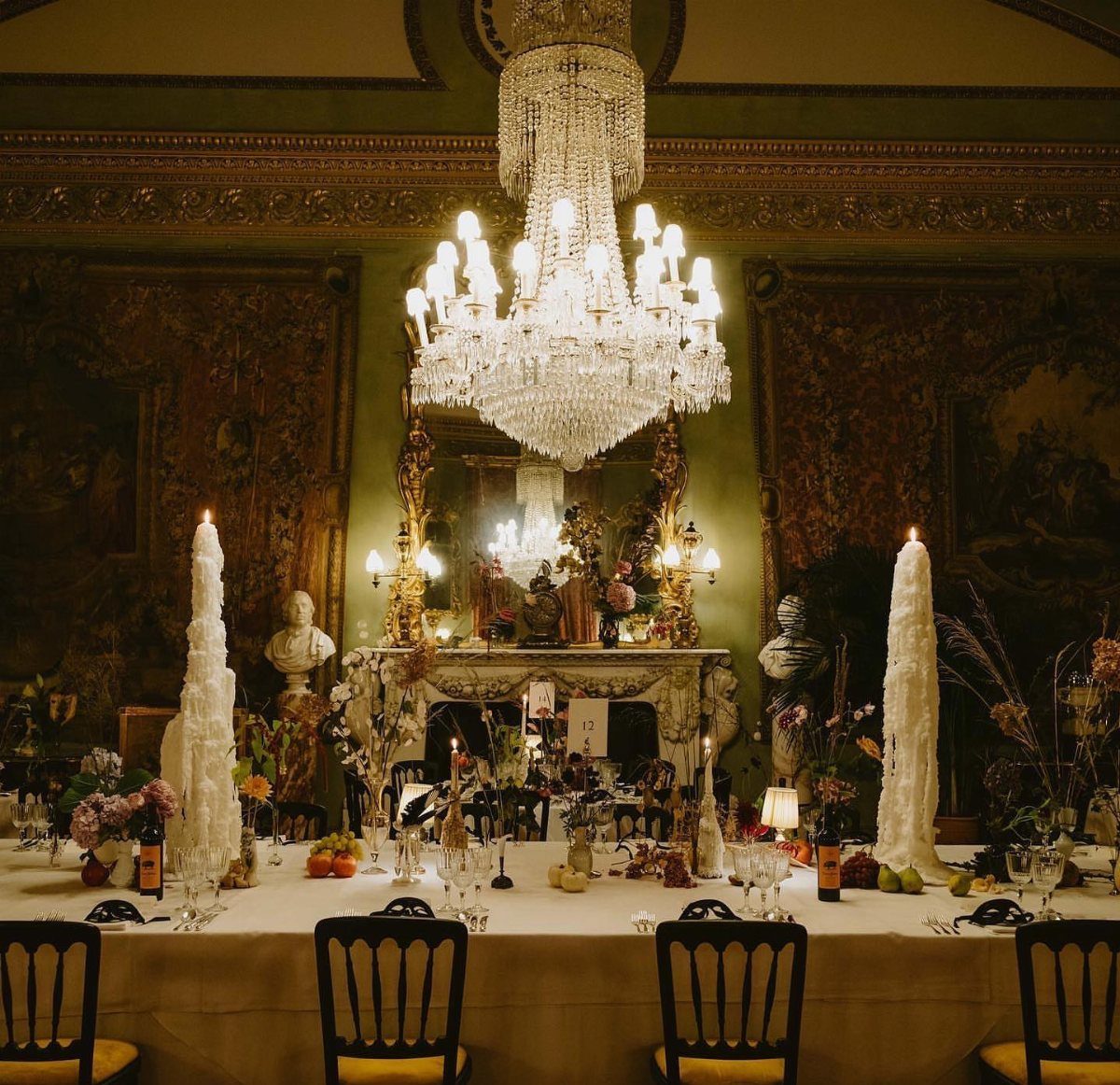 A formal dining table set with tall white candles under a large crystal chandelier.