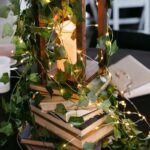 A wooden lantern with a lit candle sits on a stack of old books wrapped in ivy.