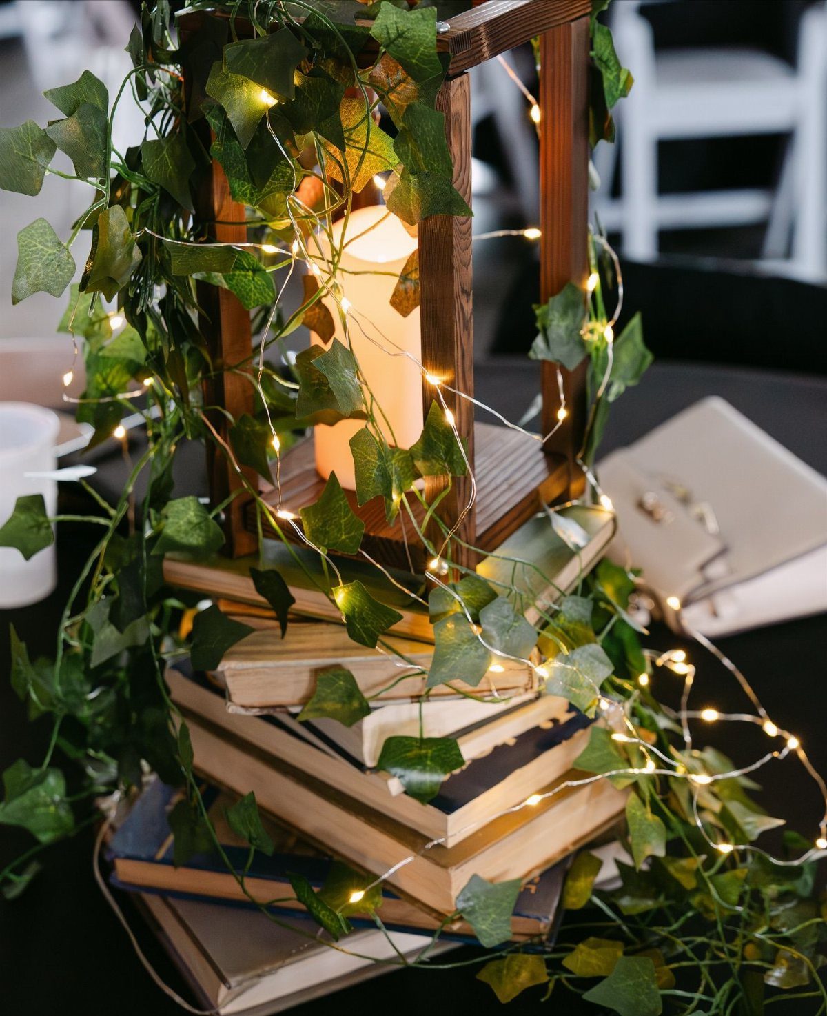 A wooden lantern with a lit candle sits on a stack of old books wrapped in ivy.