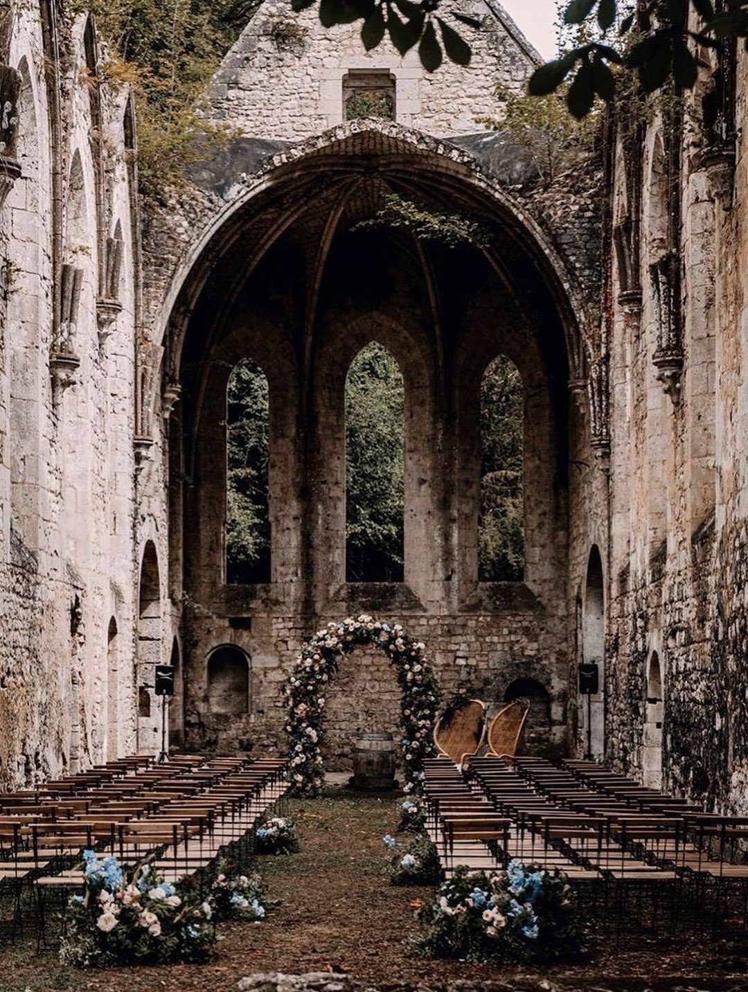 Wedding ceremony setup with wooden chairs and a floral arch inside ancient stone abbey ruins.