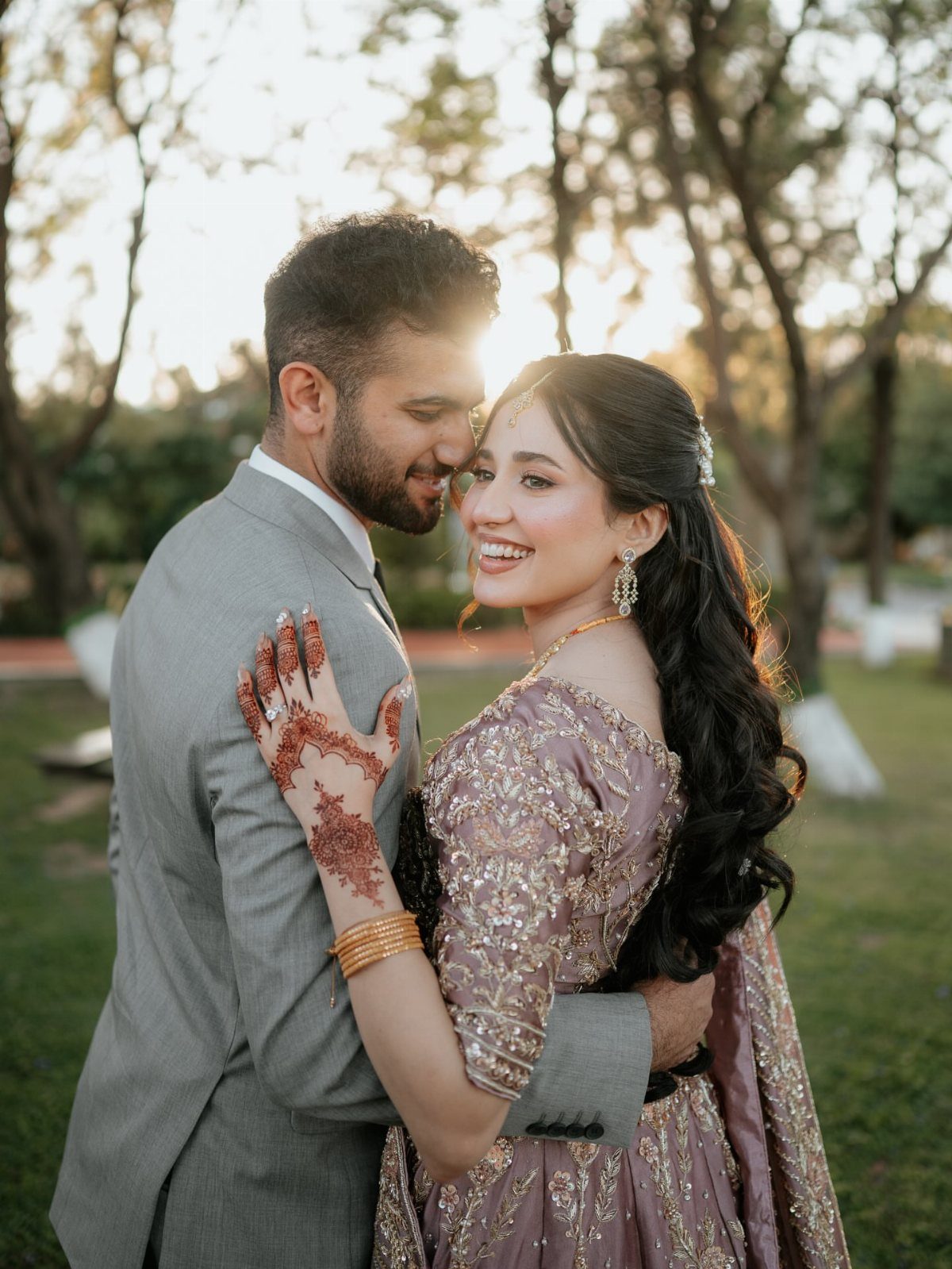 A smiling couple embracing closely in a sunlit outdoor setting during golden hour.