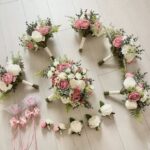 Dusty rose and cream floral bouquets and boutonnieres arranged on a light wooden surface.