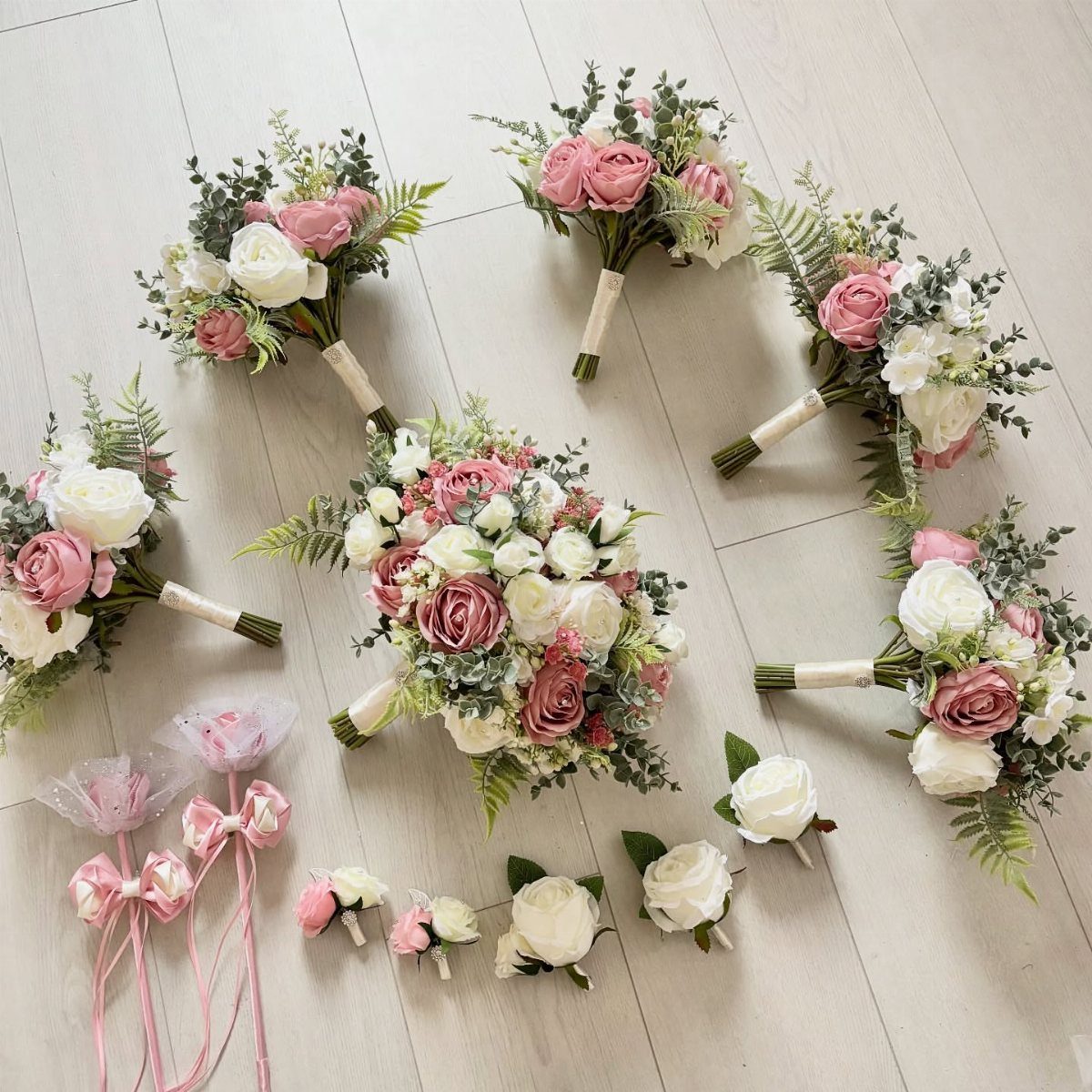 Dusty rose and cream floral bouquets and boutonnieres arranged on a light wooden surface.