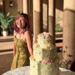 A three-tiered pale yellow cake decorated with colorful spring flowers on a white stand.