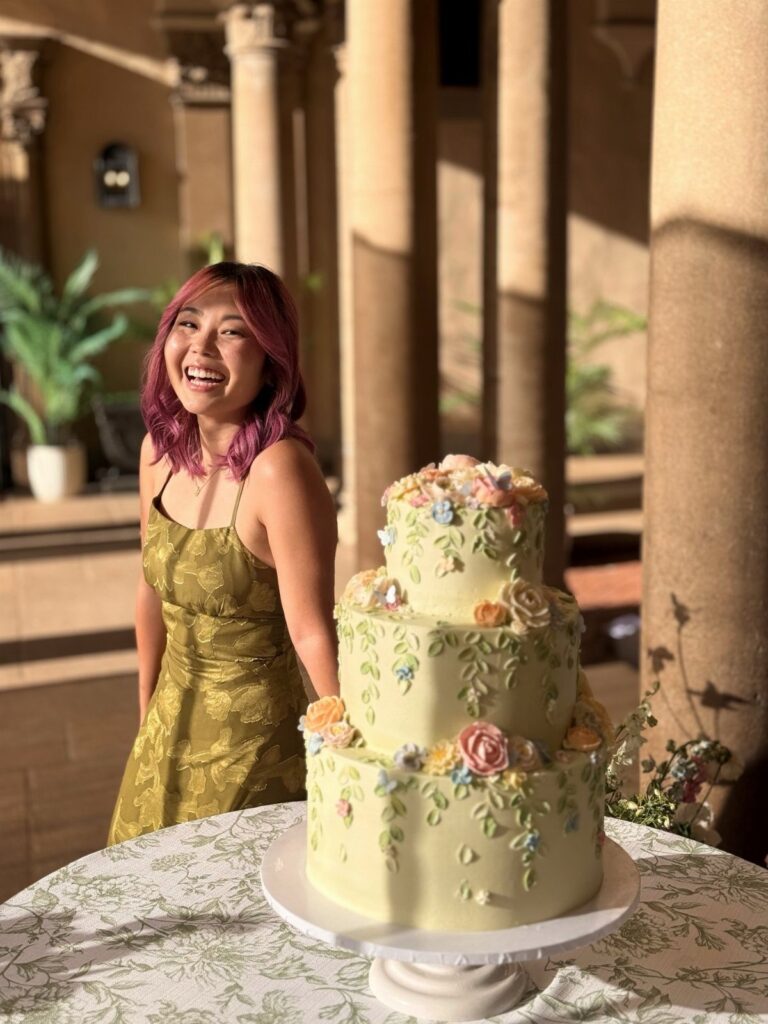 A three-tiered pale yellow cake decorated with colorful spring flowers on a white stand.