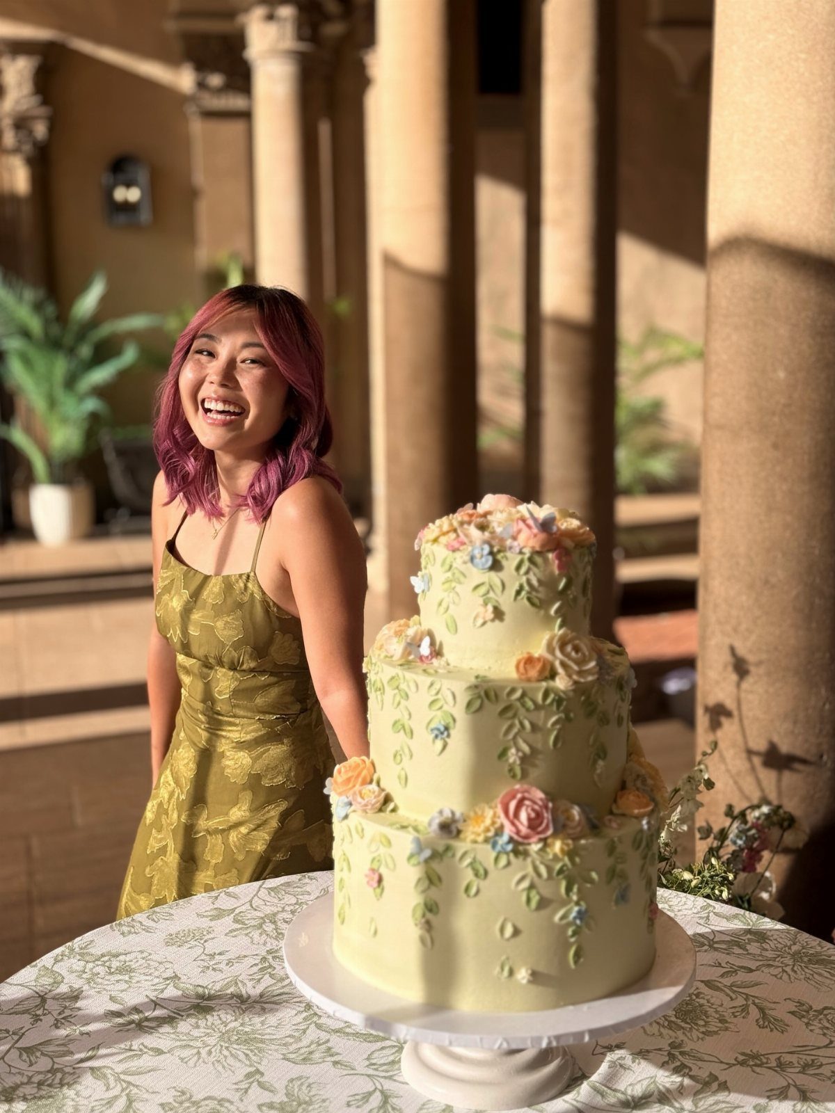A three-tiered pale yellow cake decorated with colorful spring flowers on a white stand.