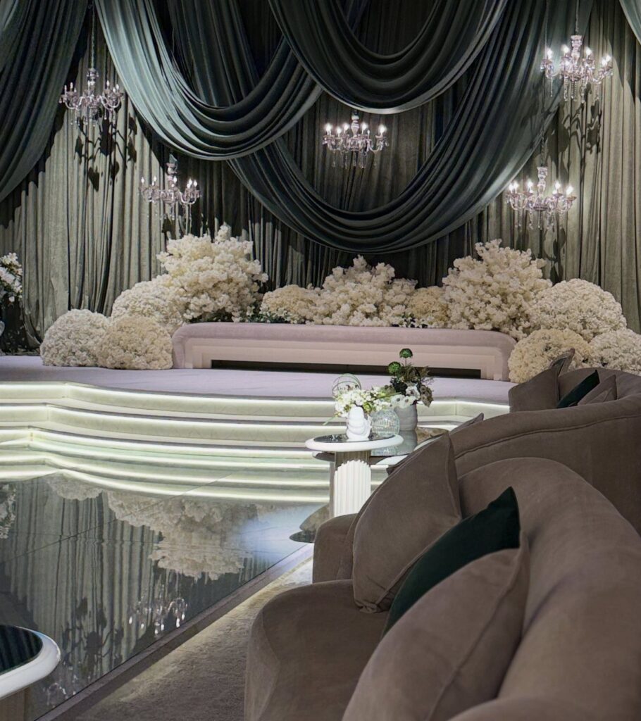 Elegant wedding stage with teal drapery, crystal chandeliers, and large white floral arrangements.