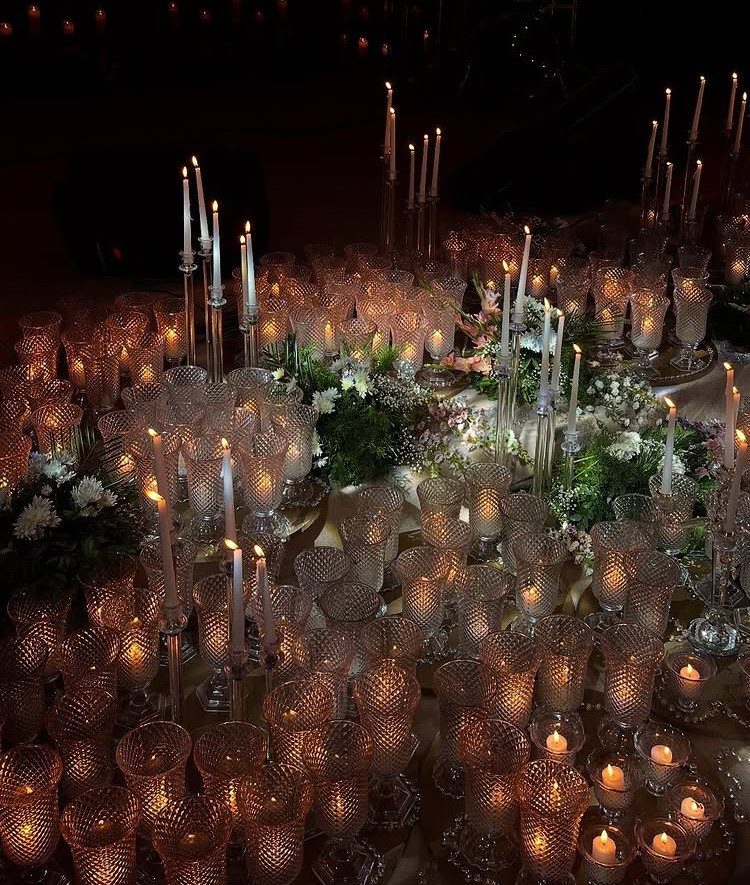Many glowing candles and glass votives arranged with greenery on a dark wedding table.