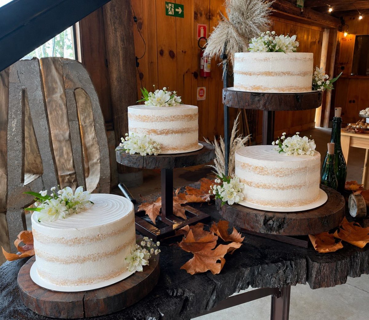 Three white naked cakes with small white flowers on rustic wooden stands atop a wooden table.