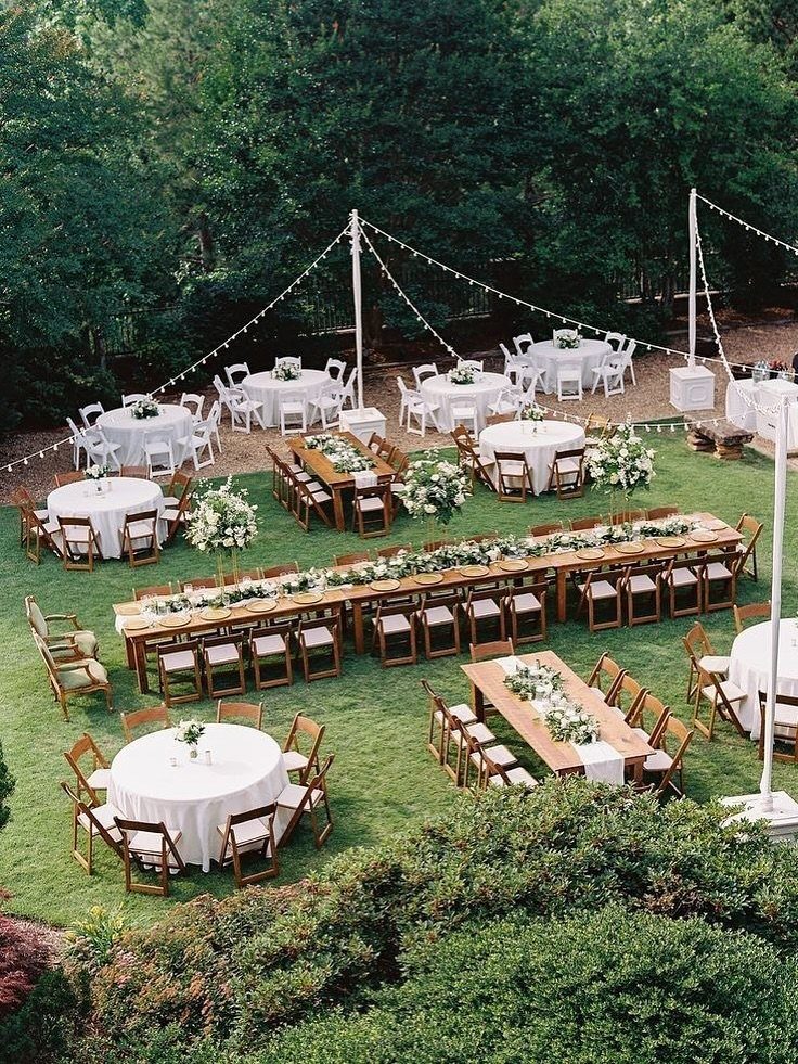 Outdoor wedding reception tables with white linens and wooden tables set on a green lawn.