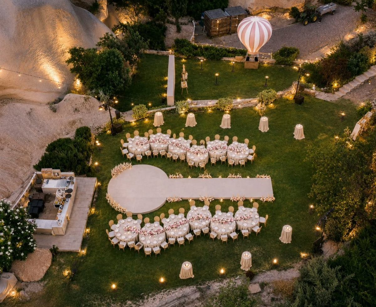 Aerial view of an outdoor wedding reception with white tables and a large dance floor on grass.